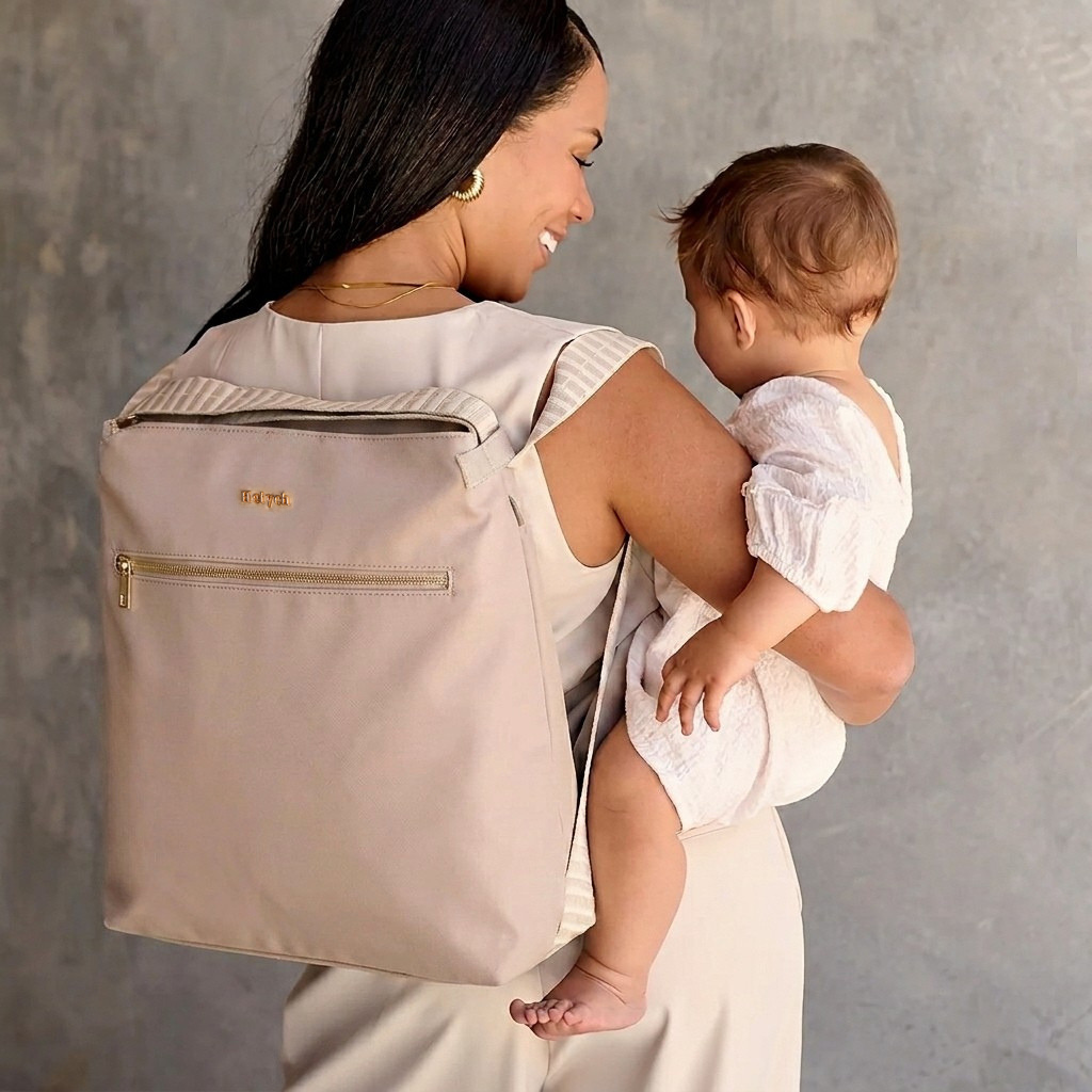 Woman carrying a baby and a beige backpack with a Heiych brand logo against a gray background