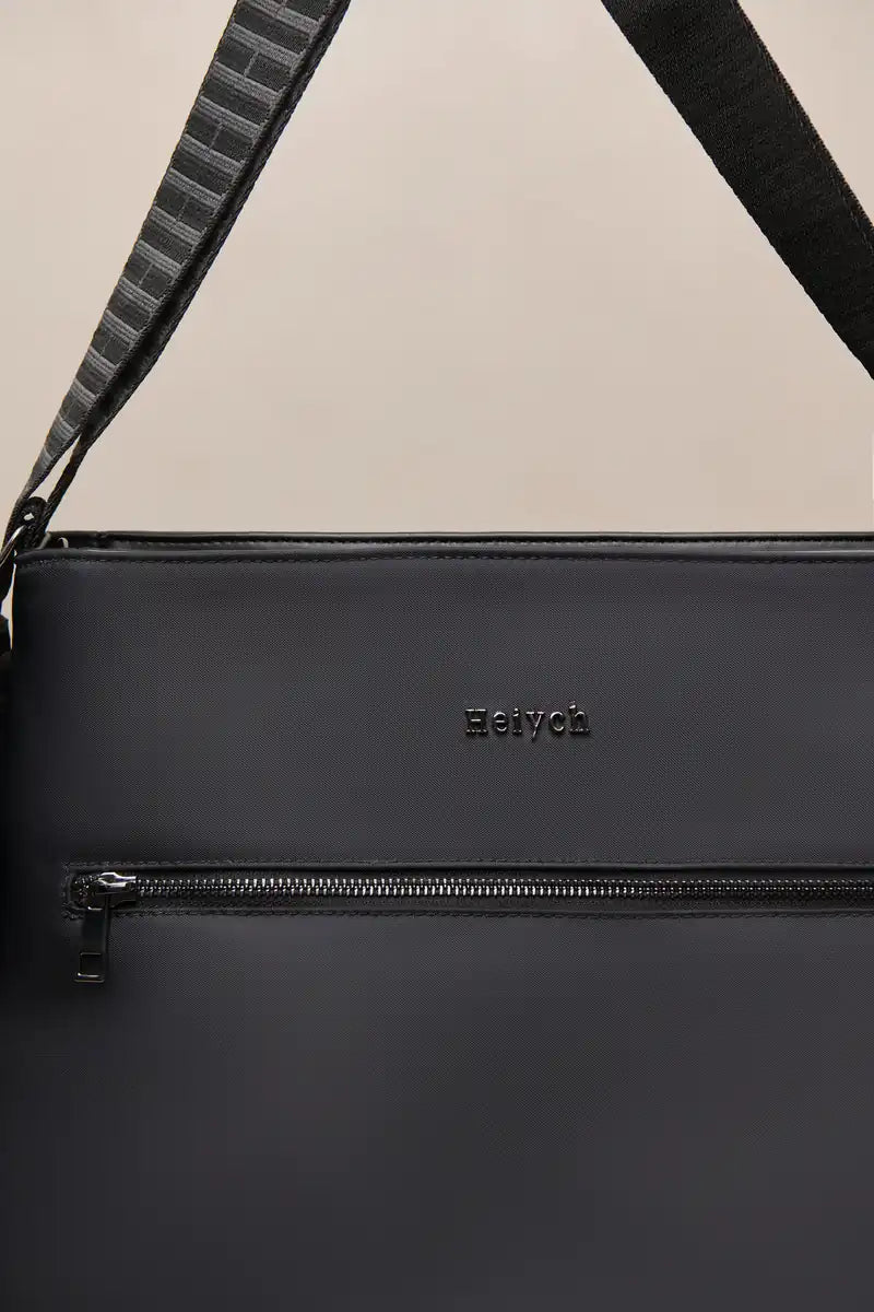 Close-up of a black nylon shoulder bag with a horizontal zippered pocket and a black-and-gray patterned strap, featuring the embossed brand name 'Heiych' on the front.
