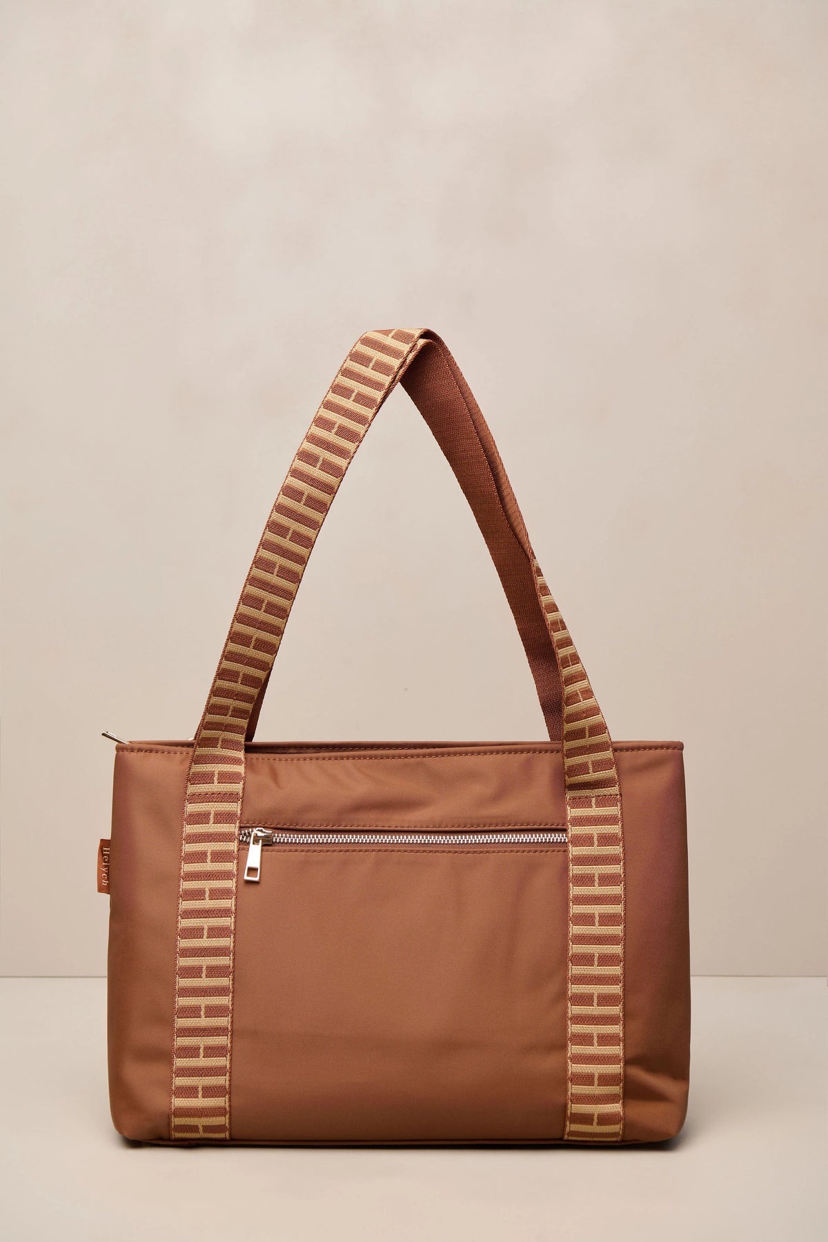 A cognac nylon tote bag with patterned beige and brown shoulder straps, shown against a neutral beige background.